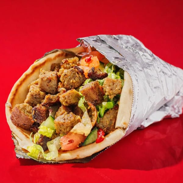 A gyro wrap filled with meat, lettuce, tomatoes, and cucumbers, partially wrapped in foil.