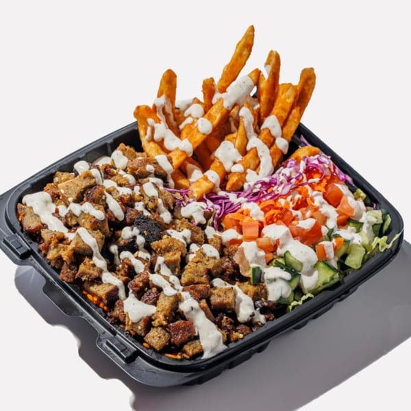 A black takeout container filled with shawarma, fries, and salad, all drizzled with white sauce.