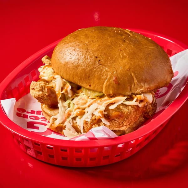 Crispy fried chicken sandwich with coleslaw, pickles, and sauce in a red basket.
