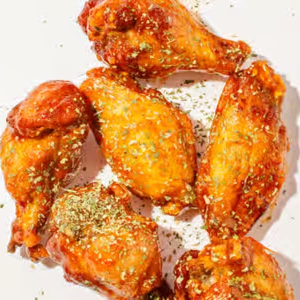 Six glazed chicken wings, sprinkled with green herbs, on a white surface.