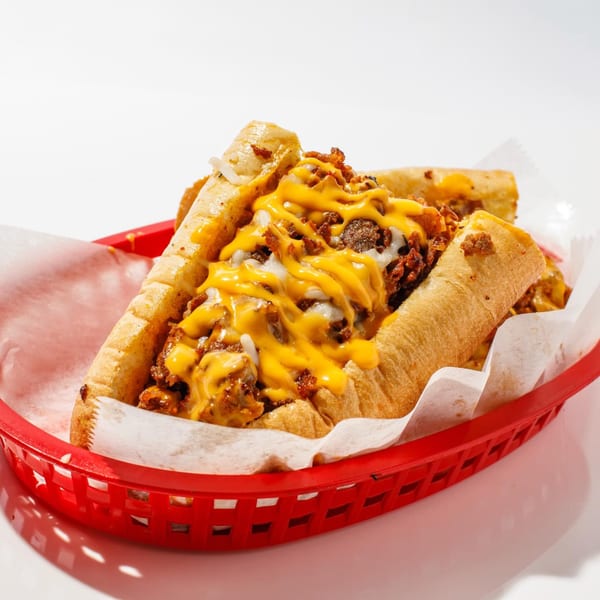 Two cheesesteak sandwiches with melted cheese and meat in a red basket lined with white paper.