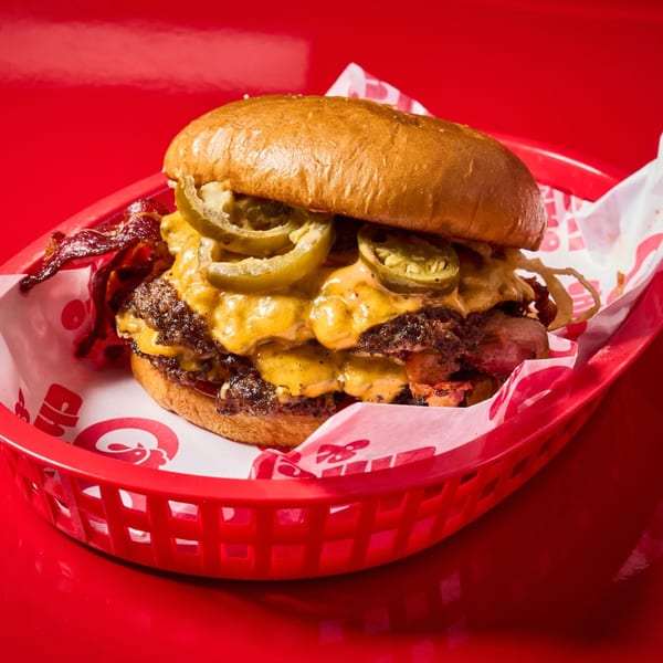 Double cheeseburger with melted cheese, jalapeños, bacon, and crispy onions in a red basket.