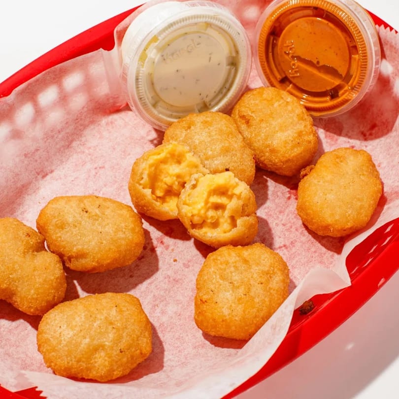 Golden-brown mac and cheese bites in a red basket with two dipping sauces.